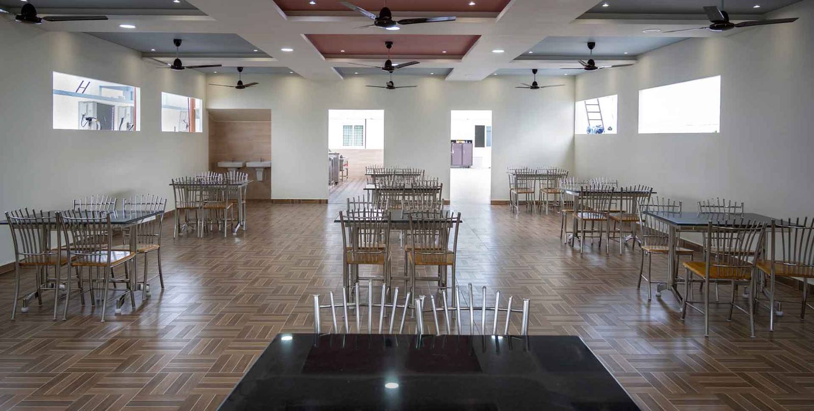The Bhojanalaya dining hall with wooden-look flooring and steel tables set for guests